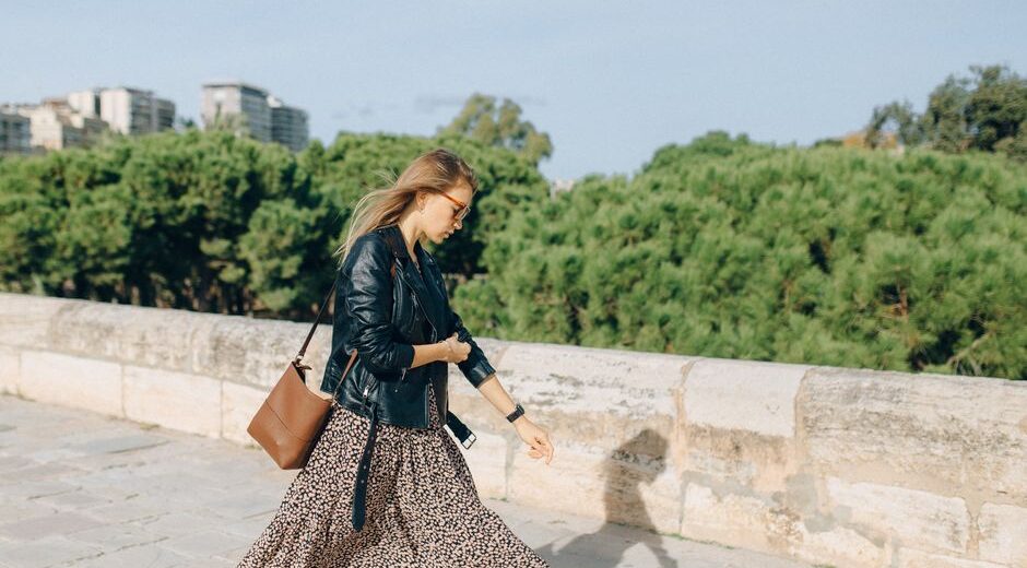 Woman wearing a black crossbody bag walking through a sunny European city street, hands-free.
