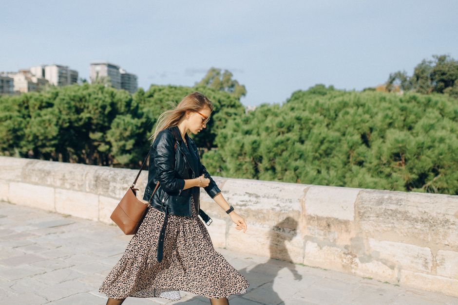 Woman wearing a black crossbody bag walking through a sunny European city street, hands-free.