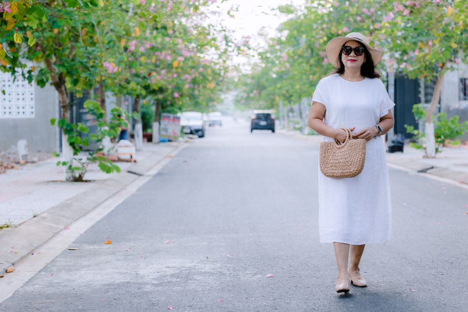 Woman elegantly walking through a sunny European street in a loose-fitting linen dress, showcasing breathable summer fashion.